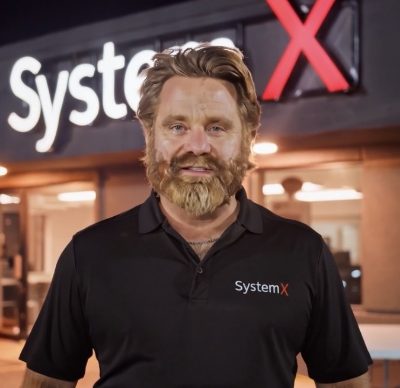 Portrait of JR Ferguson at night in front of the lit SystemX sign
